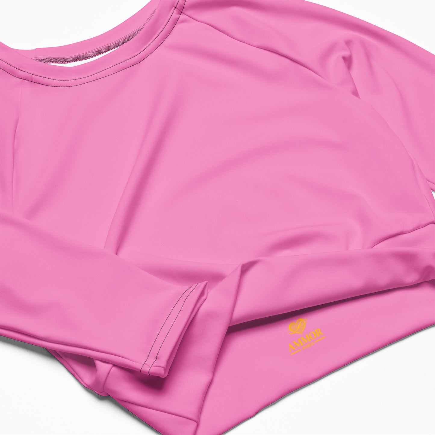 AMMOR PARIS recycled long‑sleeve crop top in bold pink, laid flat on a deep black background to showcase its UPF50+ recycled performance fabric, sculpted cropped silhouette, raglan sleeves and wide double‑layered waistband, reflecting the brand’s elevated Paris‑born sustainable athletic aesthetic.
